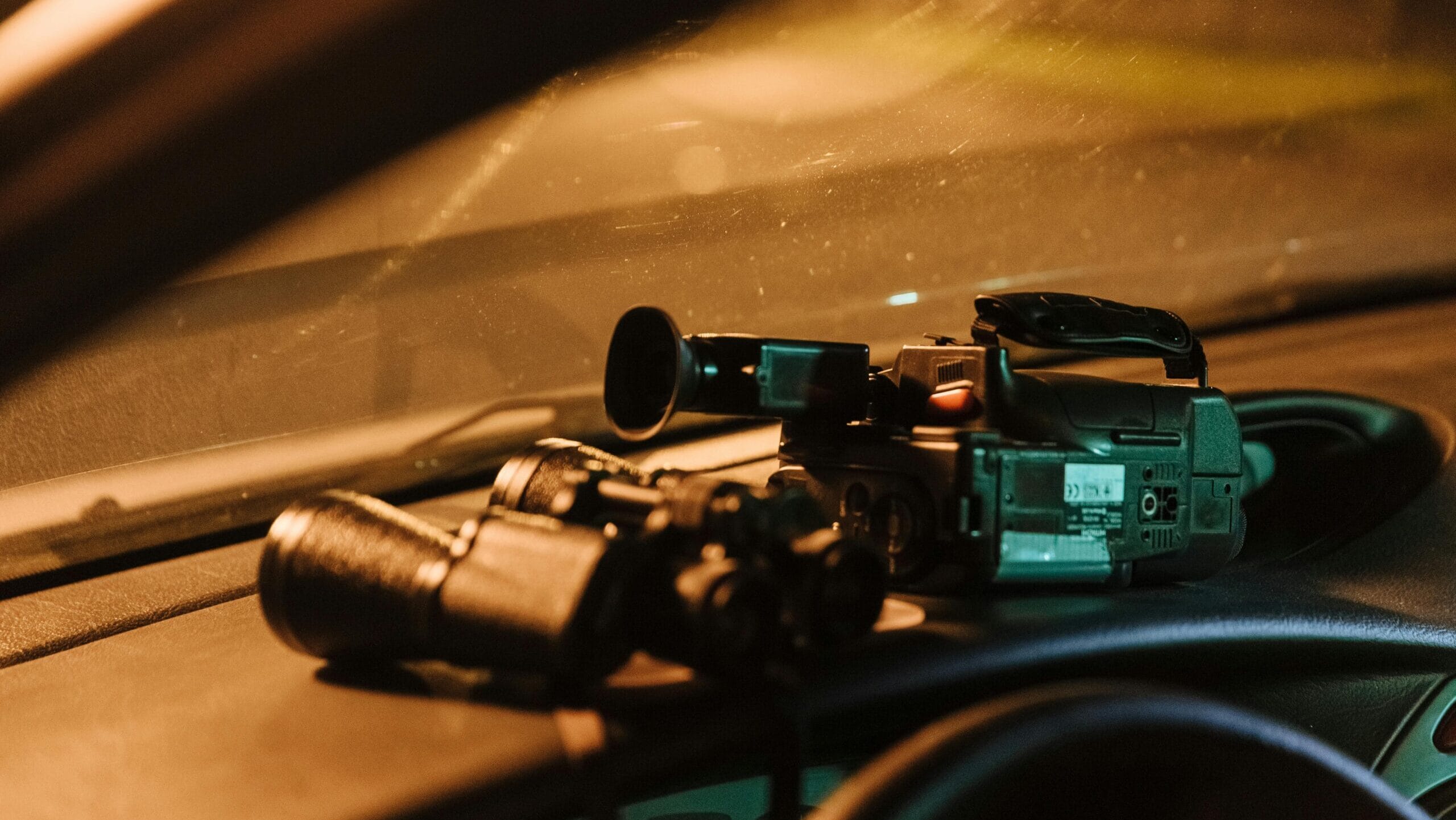 Close-up of a camcorder and binoculars on car dashboard captured at night.