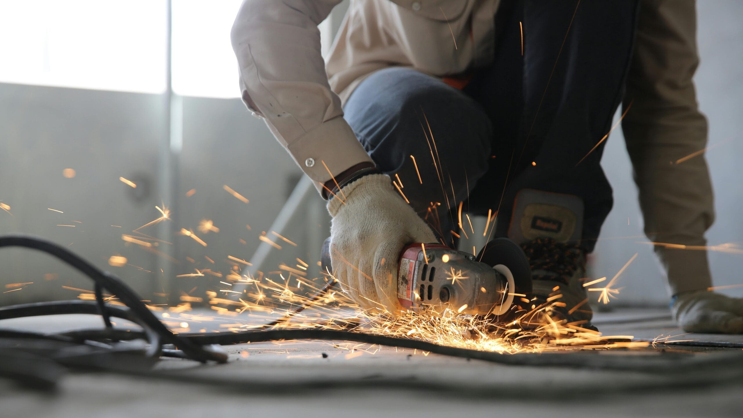 A skilled industrial worker uses a grinder creating a burst of sparks indoors.