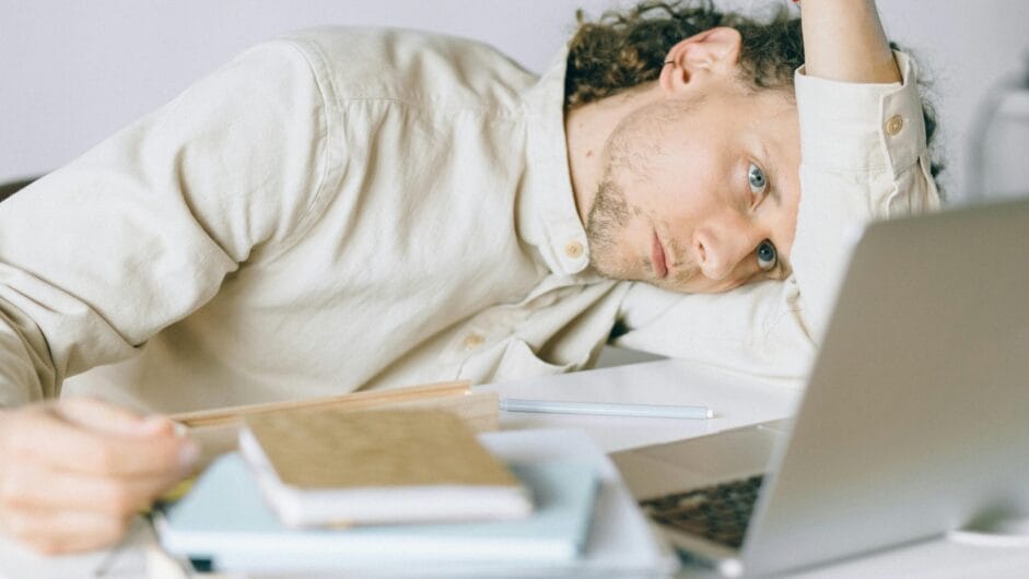 A tired Caucasian man at a desk, showing signs of exhaustion and stress, exemplifying workplace burnout.