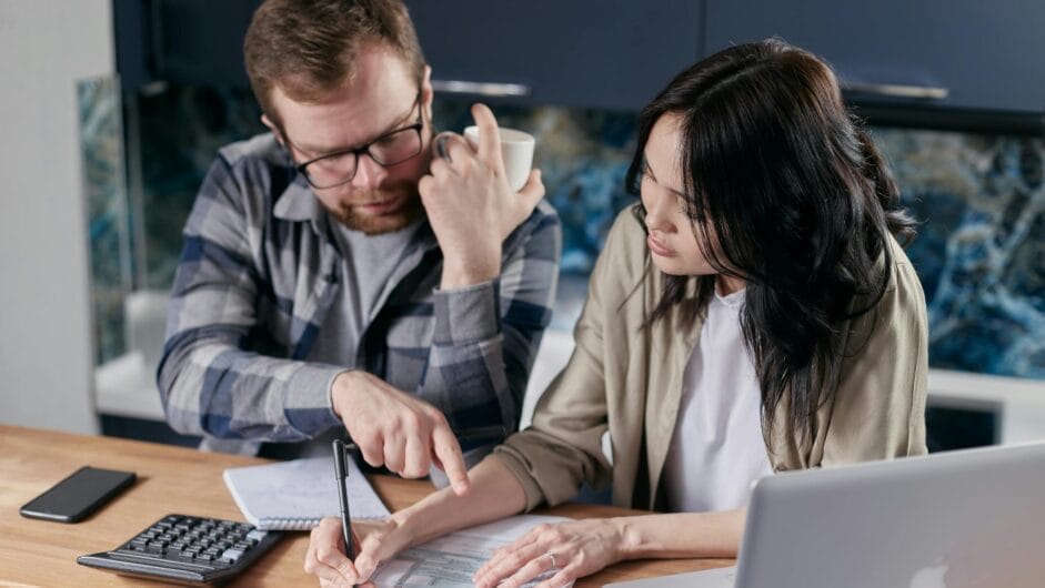 A couple analyzing financial documents with calculator and laptop on a table.